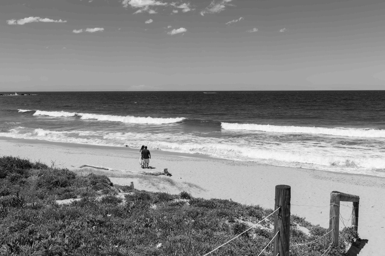 The couple seen from the dunes, small against the ocean