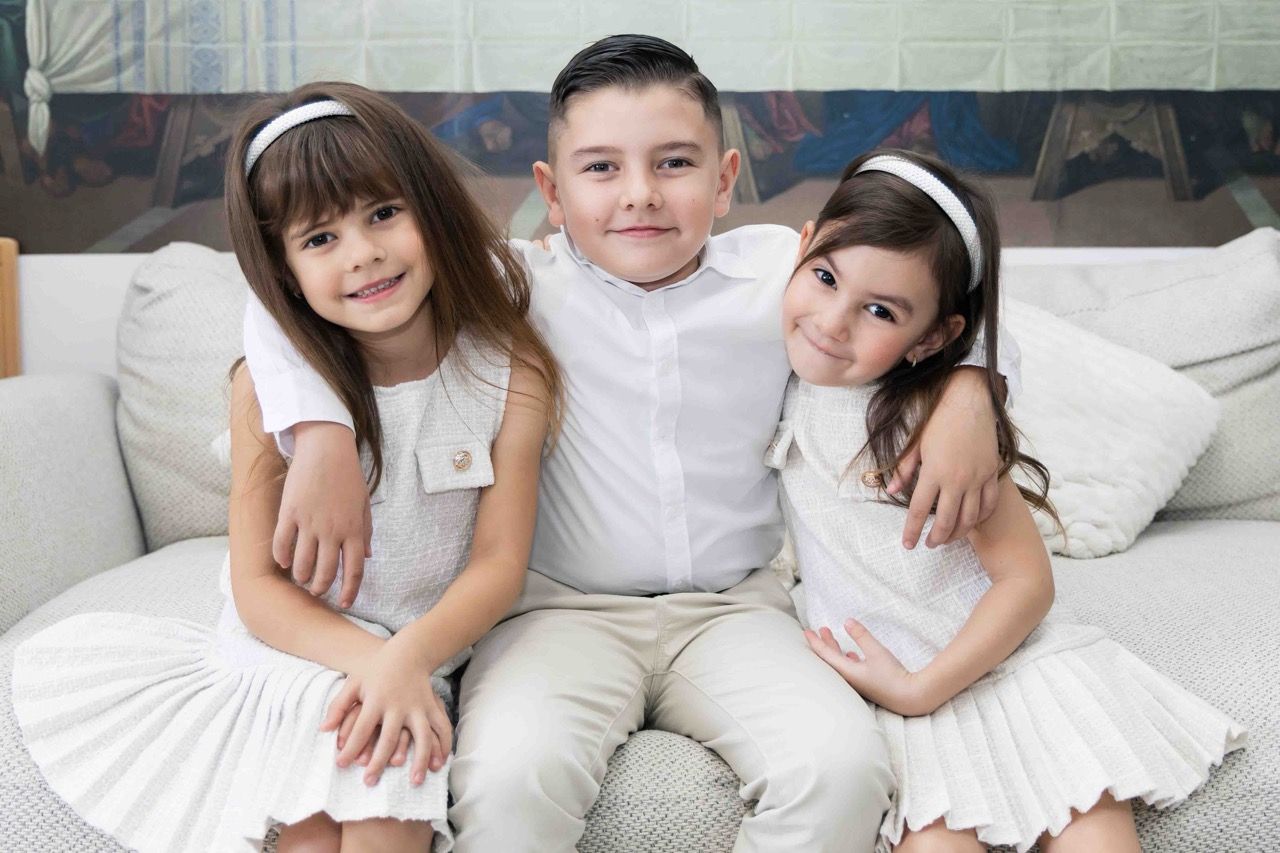 Three siblings in white sitting together on a couch