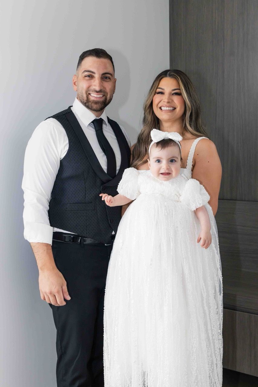 Parents stand with their baby in a lace gown