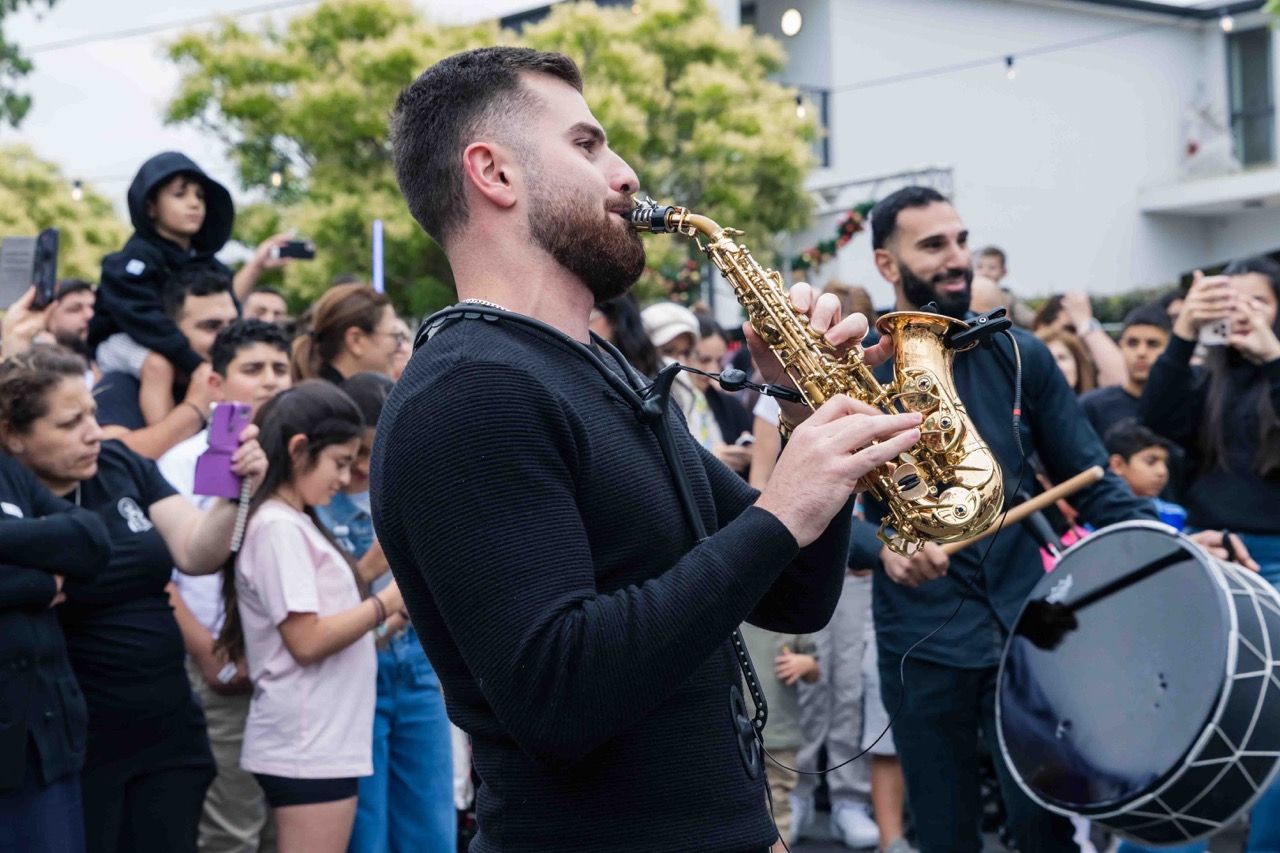 A saxophonist and drummer play to a crowd in the street