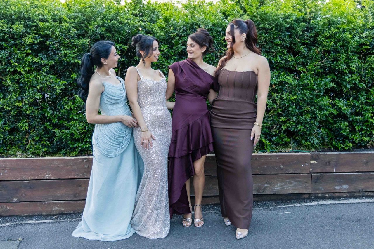 Four friends in gowns pose in front of a hedge