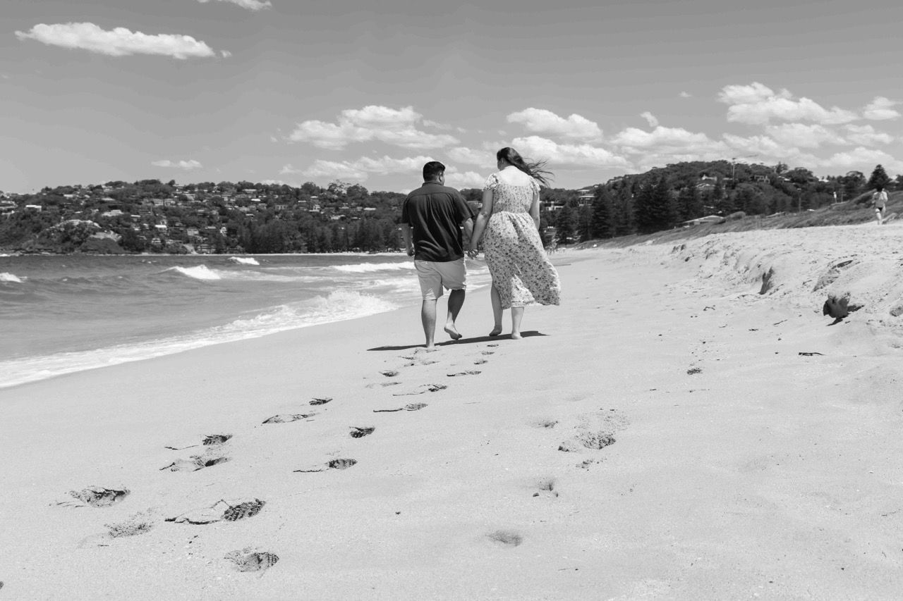 Footprints trail behind the couple walking along the beach