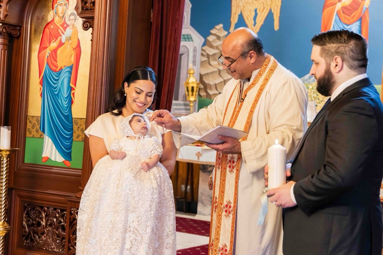 A priest blesses a baby held by her parents