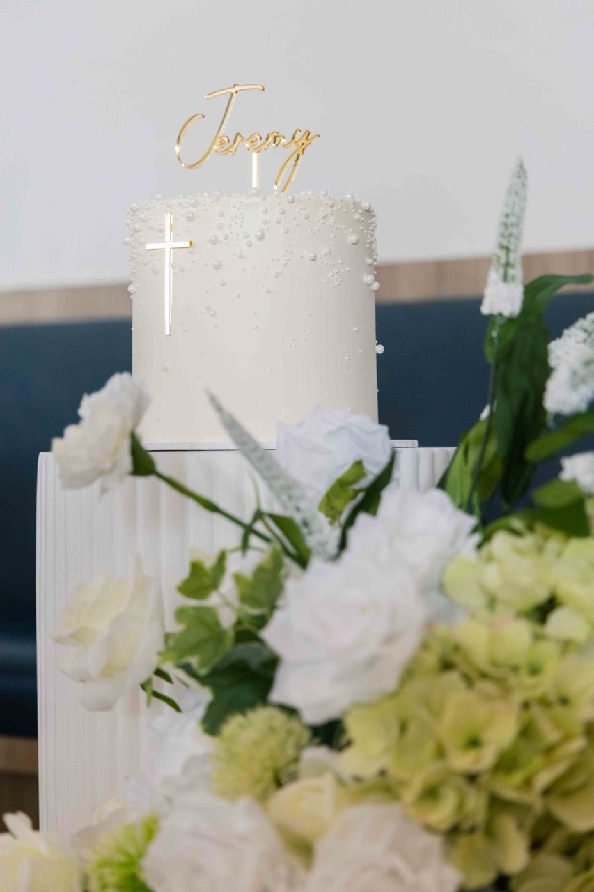 A white cake with a gold name topper among flowers
