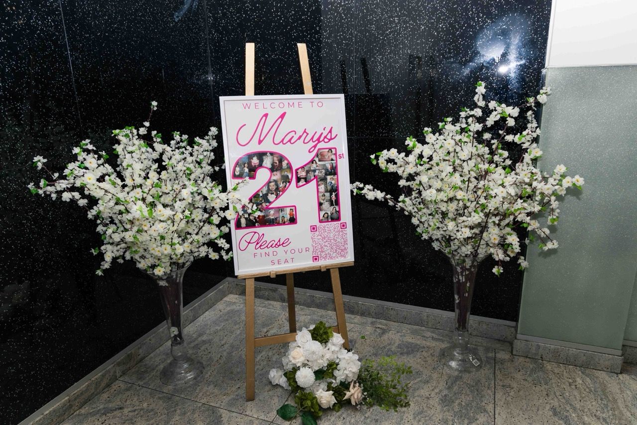 A 21st welcome sign between blossom arrangements