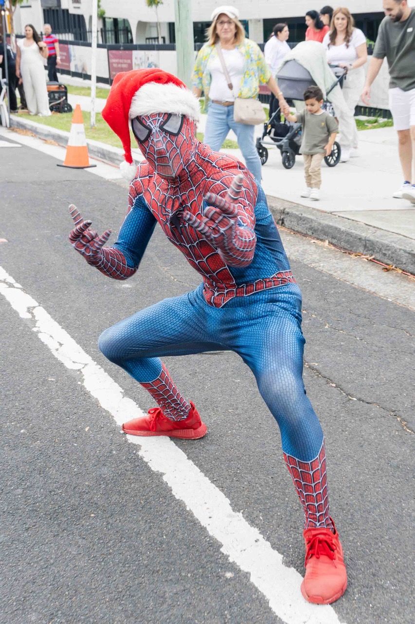 Spider-Man in a Santa hat strikes a pose on the road
