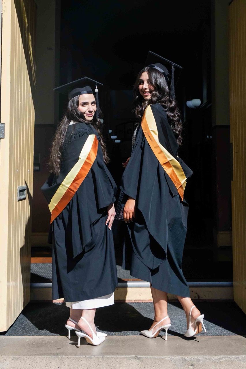 Two graduates look back over their shoulders in a doorway