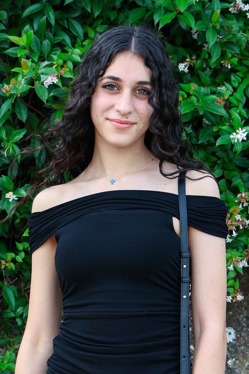 A portrait in a black off-shoulder top in front of greenery