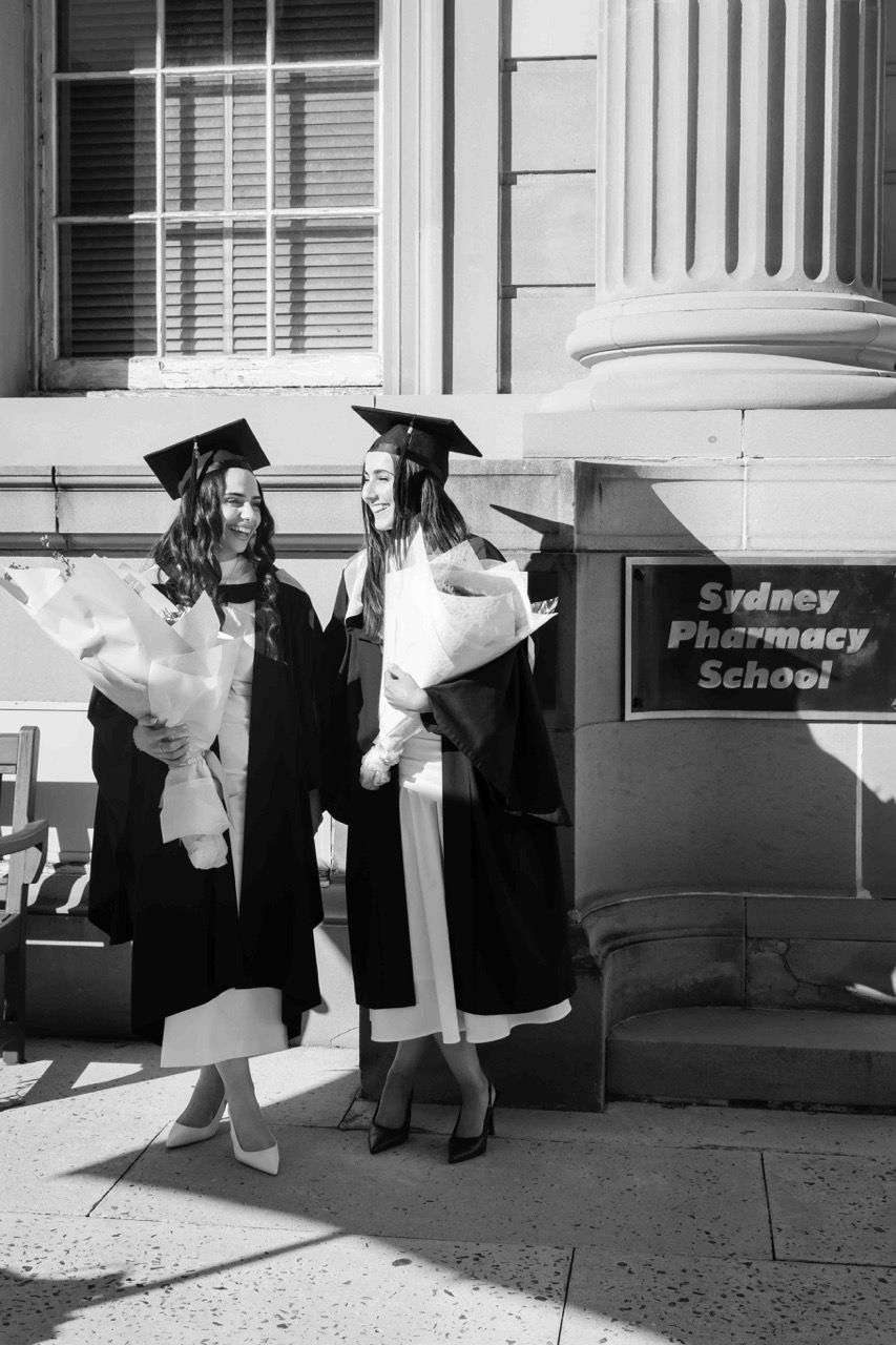 Two graduates with flowers outside the pharmacy school