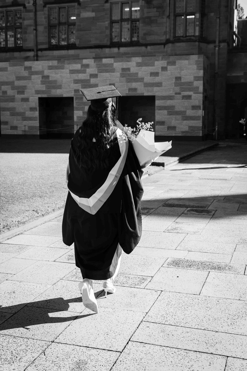 A graduate walks away across the sandstone courtyard
