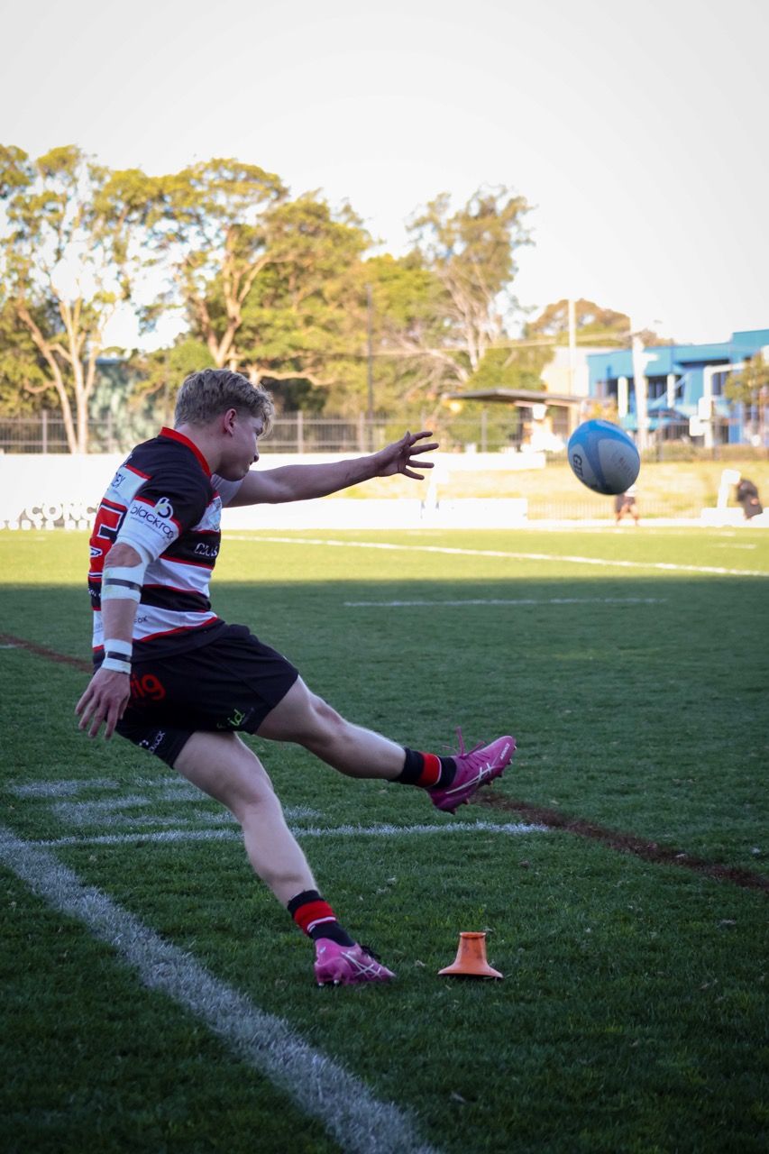A kicker follows through as the ball flies towards the posts